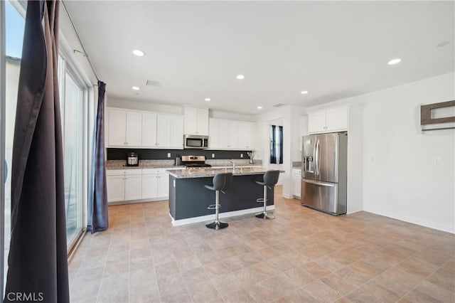 36927 Arezzo Ct, Beaumont, CA 92223 - kitchen with appliances with stainless steel finishes, a breakfast bar, white cabinets, an island with sink, and recessed lighting
