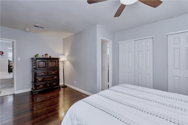 bedroom featuring baseboards, dark wood-type flooring, a ceiling fan, and multiple closets