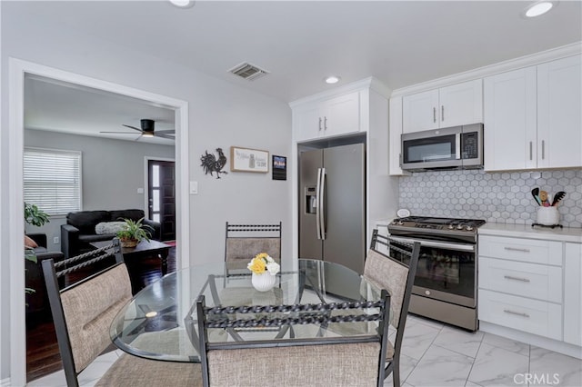 kitchen featuring stainless steel appliances, white cabinets, light countertops, decorative backsplash, and light marble finish floors
