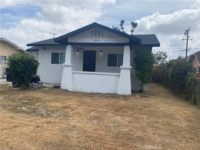 bungalow with fence, stucco siding, and a shingled roof