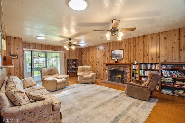 living room featuring a fireplace, a textured ceiling, ceiling fan, wood finished floors, and wood walls