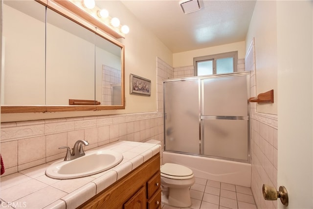 full bath with tile walls, tile patterned flooring, toilet, vanity, and bath / shower combo with glass door