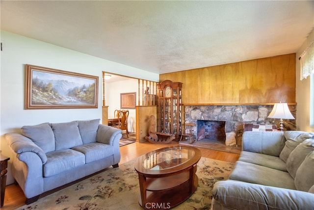 living room with wood finished floors, a stone fireplace, and wood walls