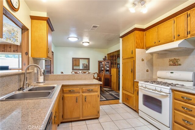 kitchen featuring gas range gas stove, under cabinet range hood, a sink, tasteful backsplash, and light tile patterned floors