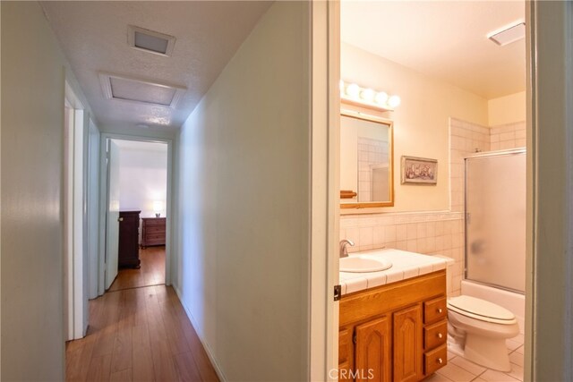 corridor featuring a sink, light wood-style flooring, and tile walls
