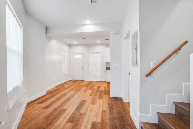 hallway with stairs, light wood-style flooring, electric panel, baseboards, and recessed lighting