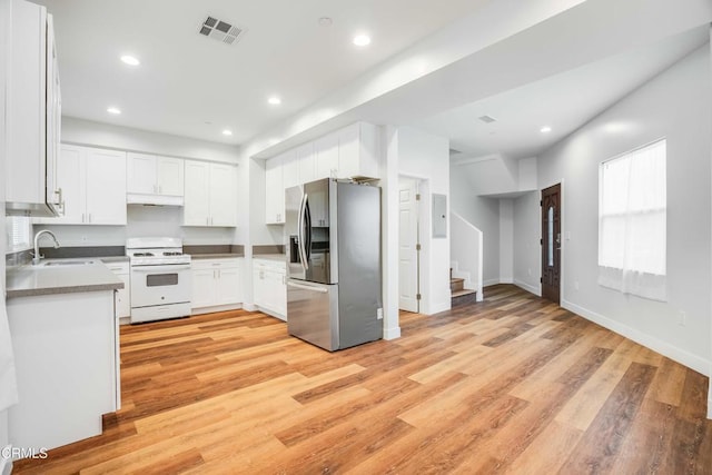 kitchen featuring stainless steel fridge, white gas range, a sink, light wood-style flooring, and white cabinets