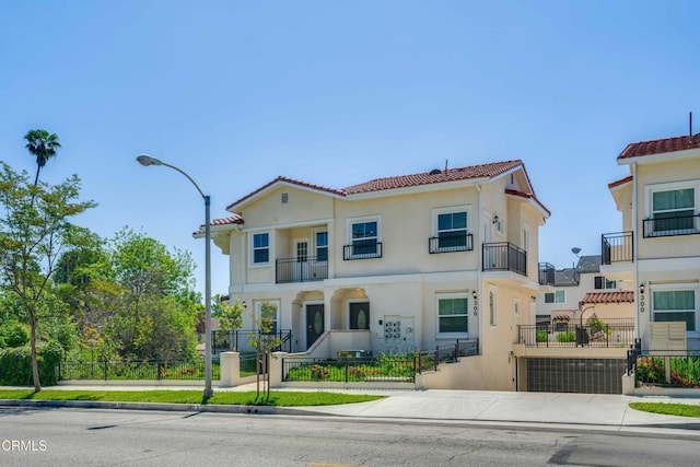 view of front of property with a fenced front yard, stucco siding, a tiled roof, a balcony, and a gate