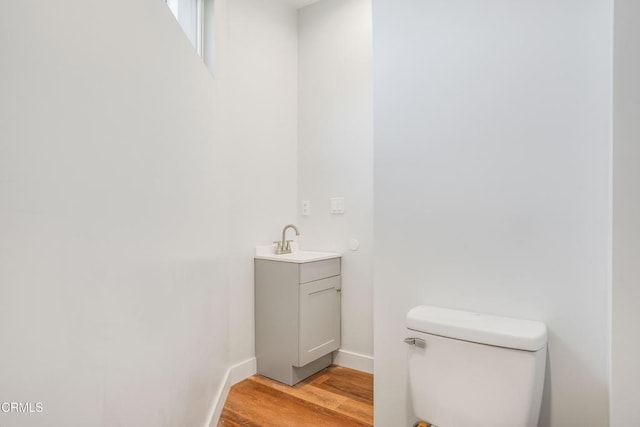 half bath with wood finished floors, toilet, vanity, and baseboards