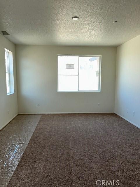carpeted empty room with a textured ceiling and baseboards