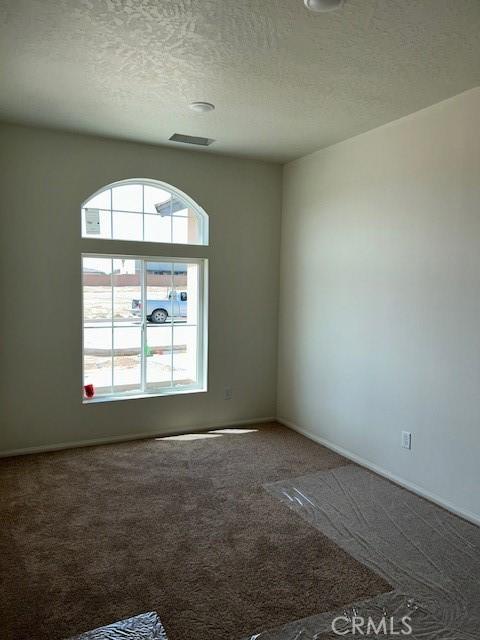carpeted spare room featuring a textured ceiling and baseboards