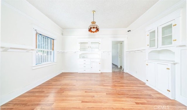 unfurnished dining area with a textured ceiling, light wood-style floors, baseboards, and ornamental molding