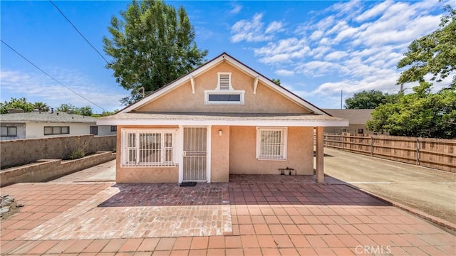 rear view of house featuring stucco siding, fence, and a patio