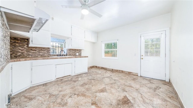 kitchen featuring white cabinets, decorative backsplash, a sink, ceiling fan, and light countertops
