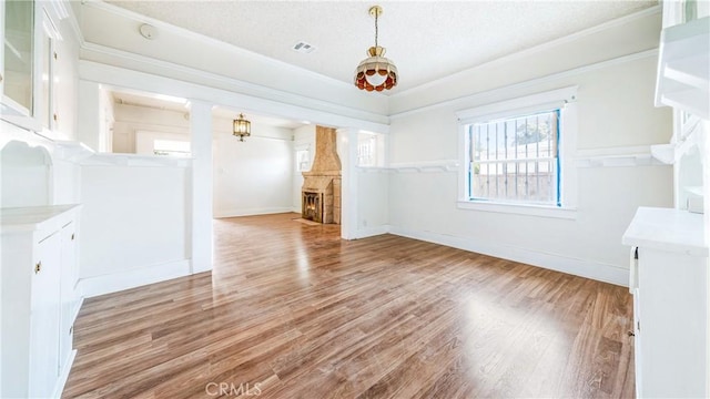 unfurnished dining area with crown molding, light wood-style flooring, ornate columns, baseboards, and a textured ceiling