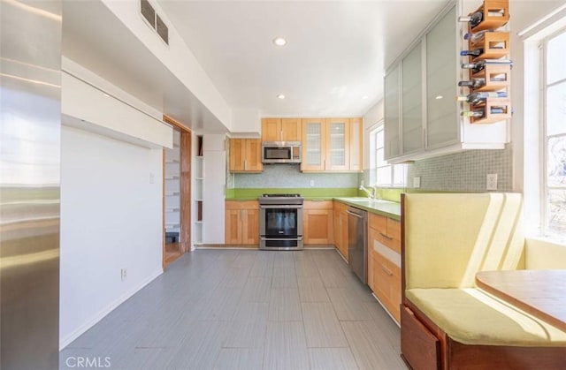kitchen with stainless steel appliances, backsplash, glass insert cabinets, a sink, and recessed lighting