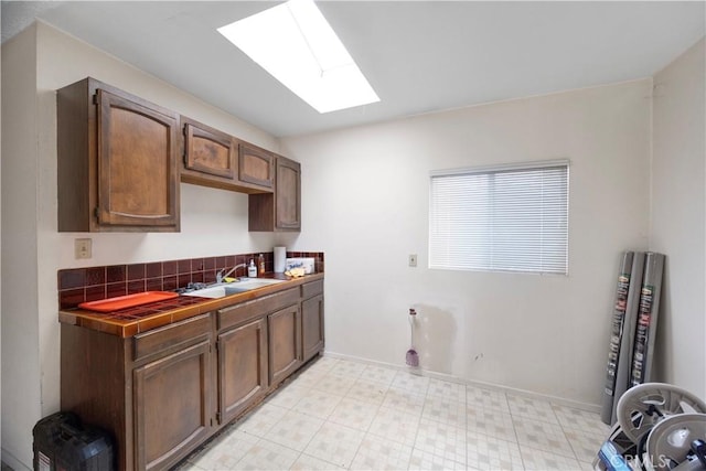 clothes washing area with a sink, a skylight, light floors, and baseboards