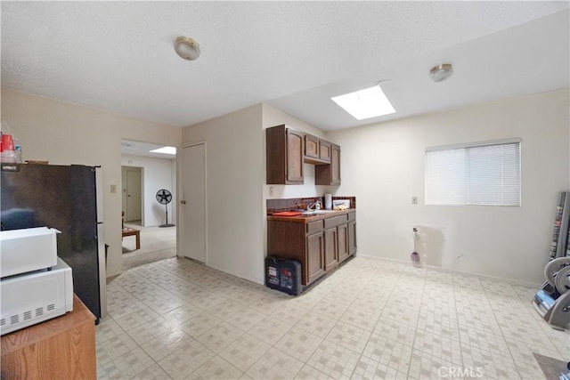 kitchen featuring a skylight, freestanding refrigerator, a sink, and baseboards