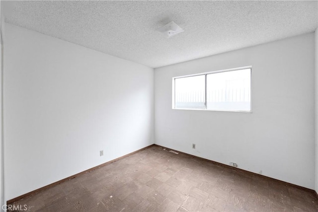 spare room featuring a textured ceiling and baseboards