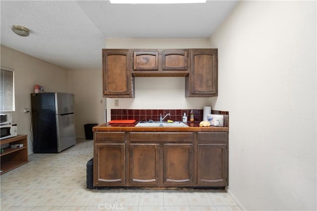 kitchen featuring freestanding refrigerator, a sink, tile countertops, white microwave, and light flooring