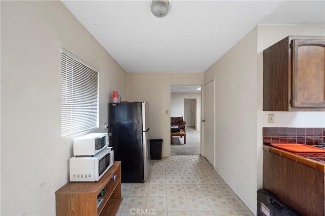 kitchen featuring freestanding refrigerator, white microwave, tile counters, and light flooring
