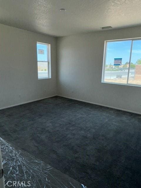 spare room with a textured ceiling, dark colored carpet, and baseboards