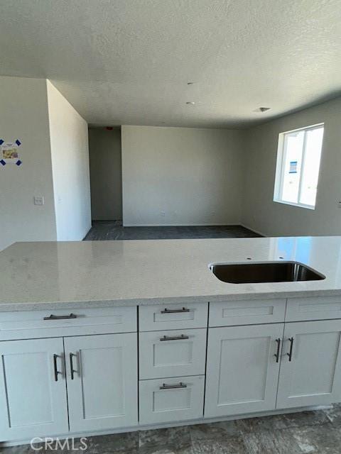kitchen featuring a textured ceiling, white cabinets, a sink, and light stone countertops