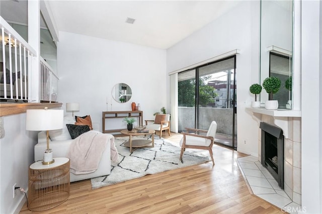 living area with light wood-style flooring, a tiled fireplace, and baseboards