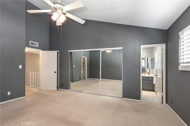 unfurnished bedroom with carpet, high vaulted ceiling, ensuite bathroom, a textured ceiling, and a ceiling fan