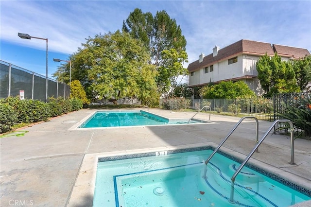 community pool with fence, a hot tub, and a patio