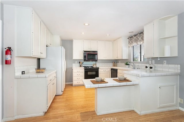 kitchen with black appliances, open shelves, a peninsula, tile counters, and light wood-style floors