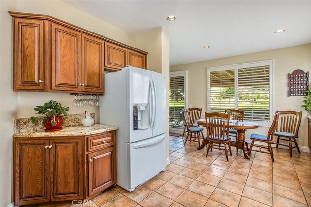 684 Big Spring Dr, Banning, CA 92220 - kitchen featuring white refrigerator with ice dispenser, brown cabinetry, light tile patterned floors, recessed lighting, and light stone countertops