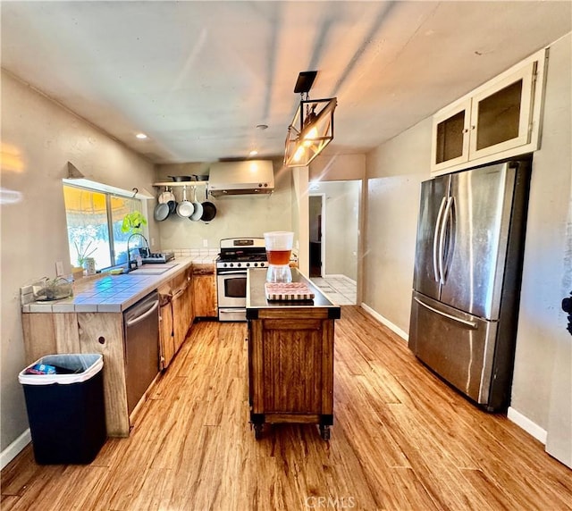 3260 E Westfall Rd, Mariposa, CA 95338 - kitchen featuring appliances with stainless steel finishes, tile countertops, light wood finished floors, wall chimney range hood, and a sink