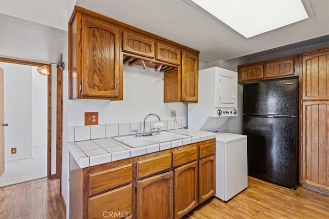 15440 Shasta Way, Pine Mountain Club, CA 93225 - kitchen featuring freestanding refrigerator, estacked washer and dryer, light wood-style flooring, and brown cabinetry