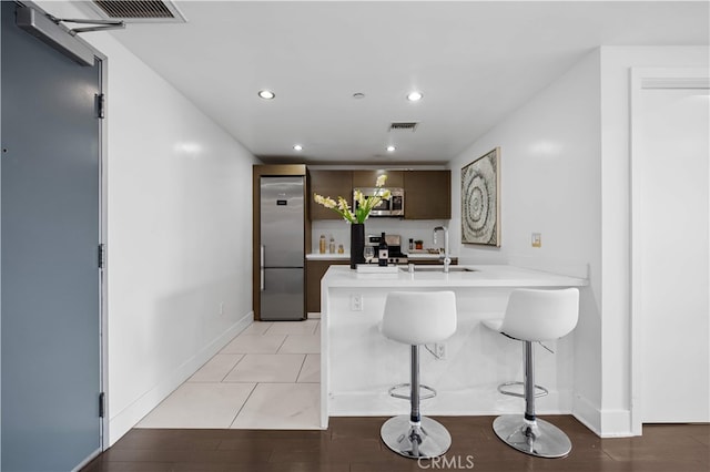 kitchen featuring appliances with stainless steel finishes, a sink, a peninsula, light countertops, and a breakfast bar area