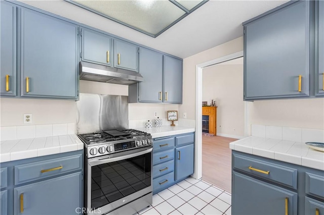 kitchen featuring stainless steel gas range, under cabinet range hood, blue cabinetry, and tile countertops