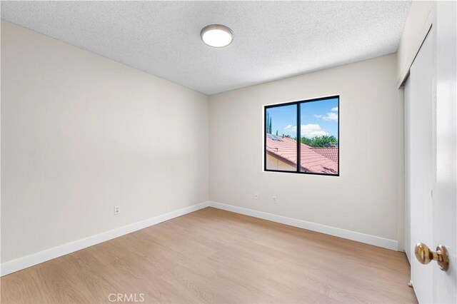spare room featuring light wood-style flooring, baseboards, and a textured ceiling