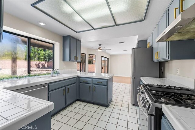 kitchen with under cabinet range hood, appliances with stainless steel finishes, a sink, a peninsula, and light tile patterned flooring
