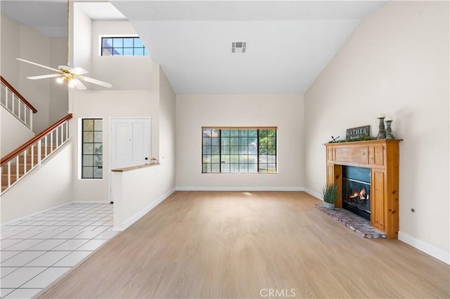 unfurnished living room featuring plenty of natural light, light wood finished floors, a glass covered fireplace, a ceiling fan, and high vaulted ceiling