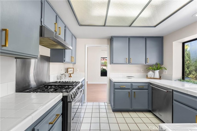 kitchen with stainless steel appliances, under cabinet range hood, tile countertops, light tile patterned floors, and gray cabinets