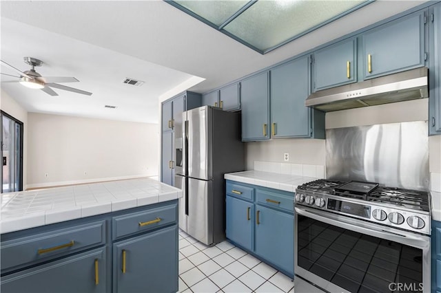 kitchen featuring stainless steel appliances, blue cabinets, under cabinet range hood, a ceiling fan, and light tile patterned flooring