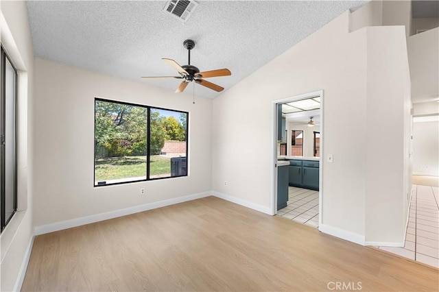 empty room with ceiling fan, a textured ceiling, light wood finished floors, vaulted ceiling, and baseboards