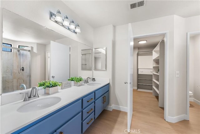 bathroom featuring wood finished floors, a stall shower, double vanity, baseboards, and toilet