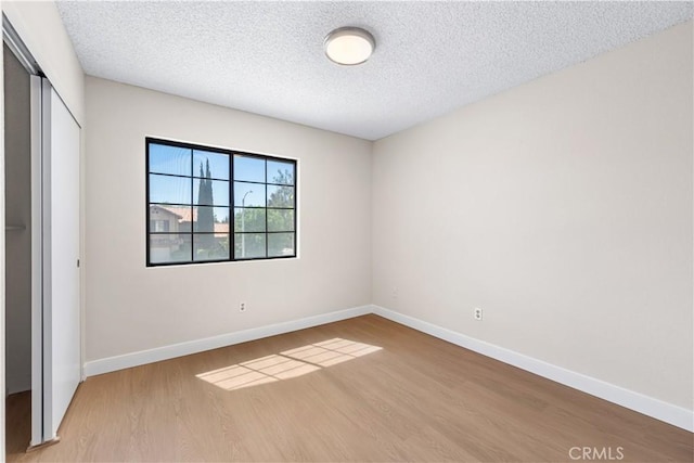 unfurnished bedroom with wood finished floors, a closet, baseboards, and a textured ceiling