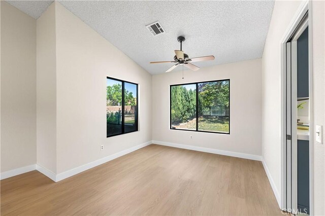 spare room featuring light wood finished floors, ceiling fan, a textured ceiling, baseboards, and vaulted ceiling