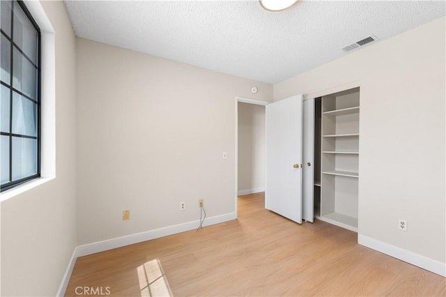 unfurnished bedroom featuring light wood-type flooring, baseboards, a textured ceiling, and a closet
