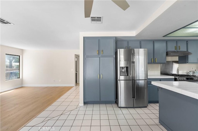 kitchen with stainless steel fridge with ice dispenser, under cabinet range hood, tile counters, stove, and light tile patterned flooring