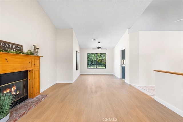 unfurnished living room with light wood-style flooring, a glass covered fireplace, a ceiling fan, lofted ceiling, and baseboards