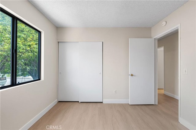 unfurnished bedroom with light wood-type flooring, a textured ceiling, a closet, and baseboards