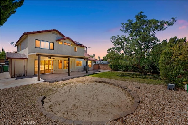 back of house at dusk with roof mounted solar panels, a patio, ceiling fan, stucco siding, and fence
